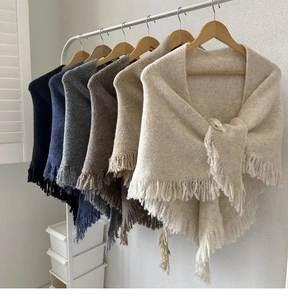 Close-up of soft wool shawls with tassels in beige, grey, and navy colors on hangers