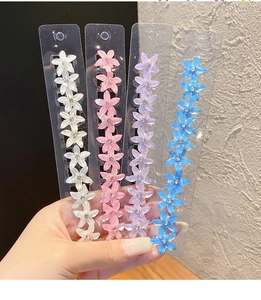 Détail de quatre pinces à cheveux fleuries en blanc, rose, violet et bleu pour filles