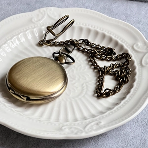 Detailed close-up of vintage bronze pocket watch with chain on white ceramic plate