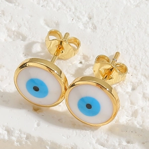 Close-up of golden evil eye stud earrings with blue enamel on a white stone surface