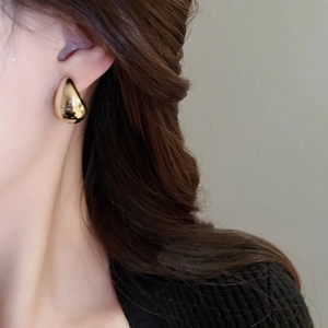Gros plan d'une boucle d'oreille dorée en forme de goutte portée par un mannequin