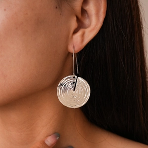 Close-up of geometric textured silver metal earrings worn by a model