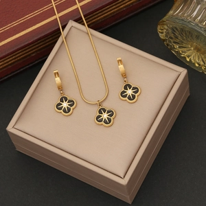 Golden flower jewelry set with black four-leaf clover star pendants on a beige box