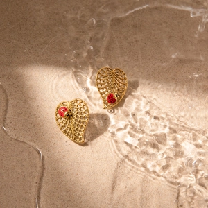 Detail of ladybug leaf earrings in gold finish over sand and water ripple background