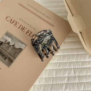 Square marble acetate hair claw clip shown on a vintage book and white quilted fabric