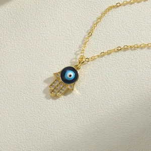 Golden Hamsa Hand necklace with evil eye pendant and zircon accents on beige background