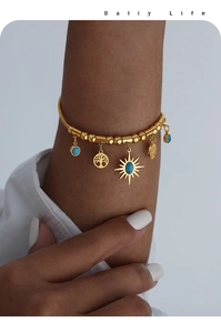 Dettaglio di bracciale dorato con ciondoli turchesi e albero della vita sul polso di donna