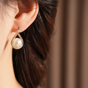 Close-up of elegant gold twisted pearl hoop earrings worn on a model's ear