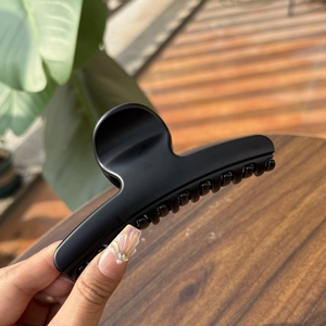 Detail of matte black large hair claw clip held by hand against a natural background