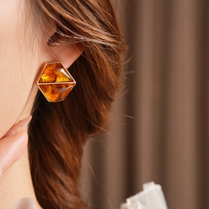Close-up of amber resin hexagonal earrings in gold frame worn by model on brown background