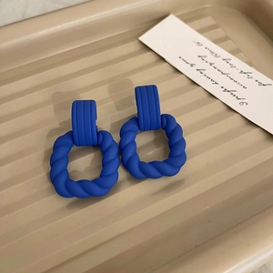 Detail view of matte Klein blue geometric earrings on a beige textured tray surface