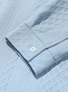 Macro shot of light blue knit cuff with geometric honeycomb texture and white button