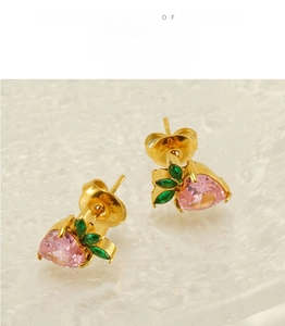 Macro detail of heart-shaped pink zircon earrings with green leaf accents on gold setting