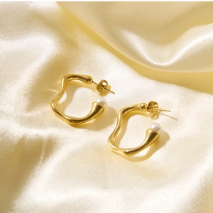Detailed shot of irregular gold hoop earrings with white pearl on silk fabric