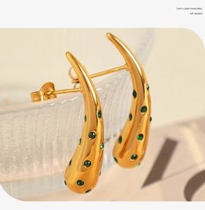 Macro shot of gold-plated teardrop earrings with green zircons on a glass edge