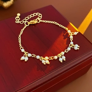 Elegante bracciale dorato con perle bianche lucide su una scatola di legno rosso scuro