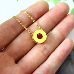 Detail of a minimalist gold donut pendant necklace held in hand for size reference