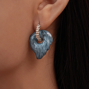 Macro shot of a silver leaf earring with a blue enamel droplet on a model's ear