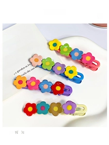 Detail of four colorful floral hair clips in pastel tones on a white textured tray