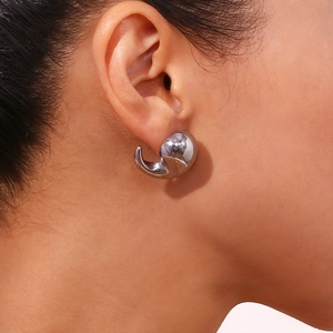 Close-up of a silver-polished curved hook stud earring worn on a model's ear