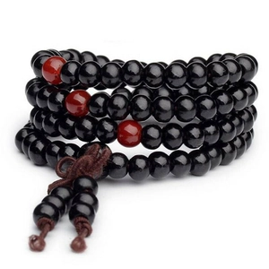 Macro detail of 108 sandalwood prayer beads with three red lucky charms on elastic cord
