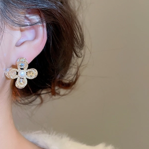 Gros plan d'une boucle d'oreille fleur en or avec pétales en zircon et perle centrale