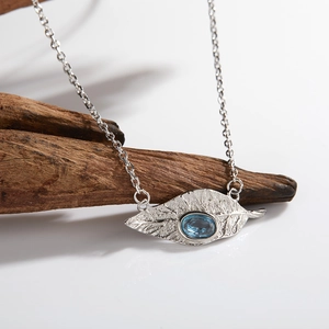 Detail of leaf design silver necklace with blue topaz stone on a rustic wooden stand