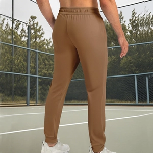 Schmal geschnittene braune Jogginghose für Herren mit Bündchen auf einem Tennisplatz