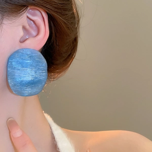 Close-up of blue brushed texture oversized irregular round earrings on female model