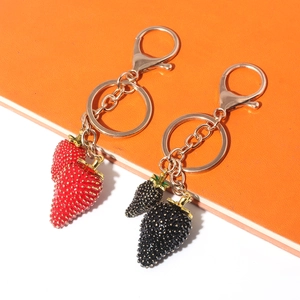 Close-up of red and black strawberry keychains with gold metal leaf and lobster clasp