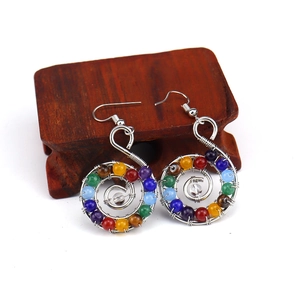 Detailed macro view of spiral wire earrings with colorful chakra beads on wood stand