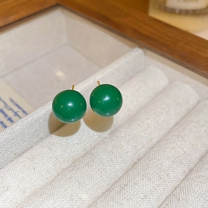 Detail of green malachite textured ball earrings with golden hooks on white jewelry box