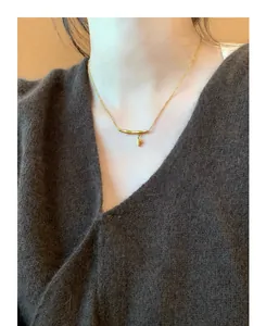 Close-up of a gold bamboo-style pendant necklace worn on a brown textured sweater