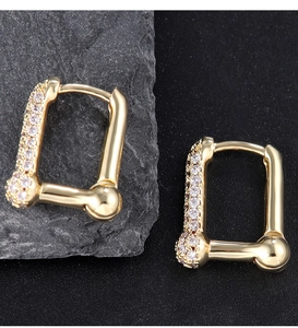 Macro shot of gold geometric earrings with pavé zircons on a textured stone surface
