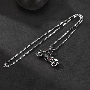 Détail du pendentif moto en argent vintage avec pierres rouges sur une chaîne en acier