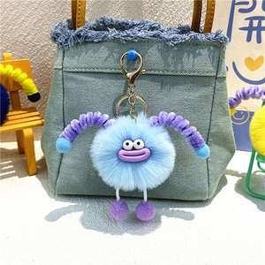 Blue plush monster keychain with big purple smile hanging on a denim bag