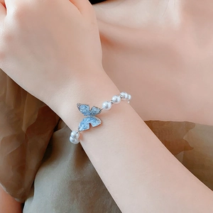 Détail d'un bracelet en perles blanches avec un pendentif papillon bleu porté au poignet