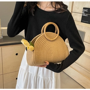 Detail of a beige semi-circular woven straw handbag with a round handle and tulip accent