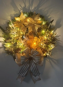 Detail of lit Christmas wreath featuring a nativity scene, pine needles, and golden flowers