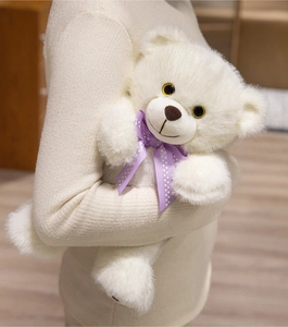 Close-up of white plush teddy bear with purple polka dot bow held in hands