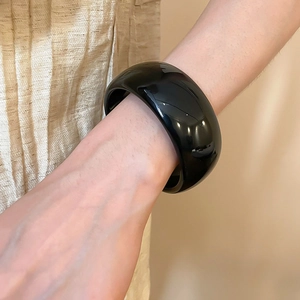 Gros plan d'un bracelet large en acrylique noir brillant porté sur un tissu doré plissé