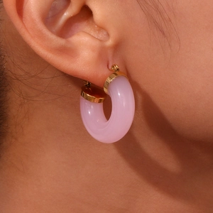 Close-up of pink acrylic C-shaped earrings with gold-plated metal tips on a model's ear