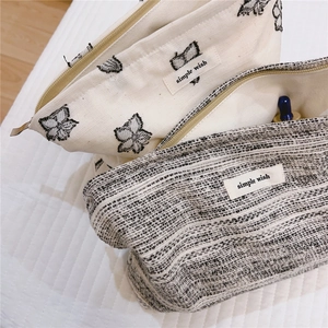 Detail of canvas makeup bags with butterfly embroidery and tweed texture zip closure