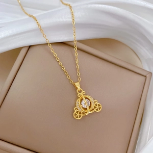 Detail of gold pumpkin carriage pendant with clear gemstone on beige jewelry box