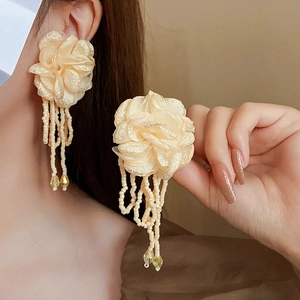 Detailed view of champagne fabric flower earrings with beaded tassels on model