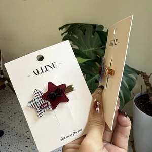 Detail showing two star-shaped hair clips with red plaid and black bows on a white card