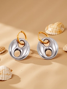 Macro view of two-tone metal earrings with organic curved silver pendant on warm sand background