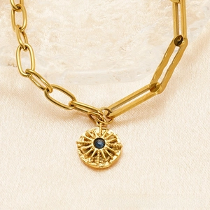 Detail of 18K gold-plated paperclip chain bracelet with a sunburst pendant and blue gemstone