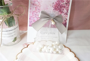 Detail of white organza pouch with grey ribbon, pearl pendant and golden ring beads