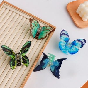 Set of four butterfly acrylic hair claws in blue and green tones on a beige tray